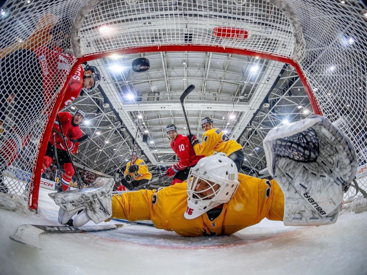 An ice hockey goalkeeper lies on the ice trying to save a goal with the photographer's camera placed inside the net. 