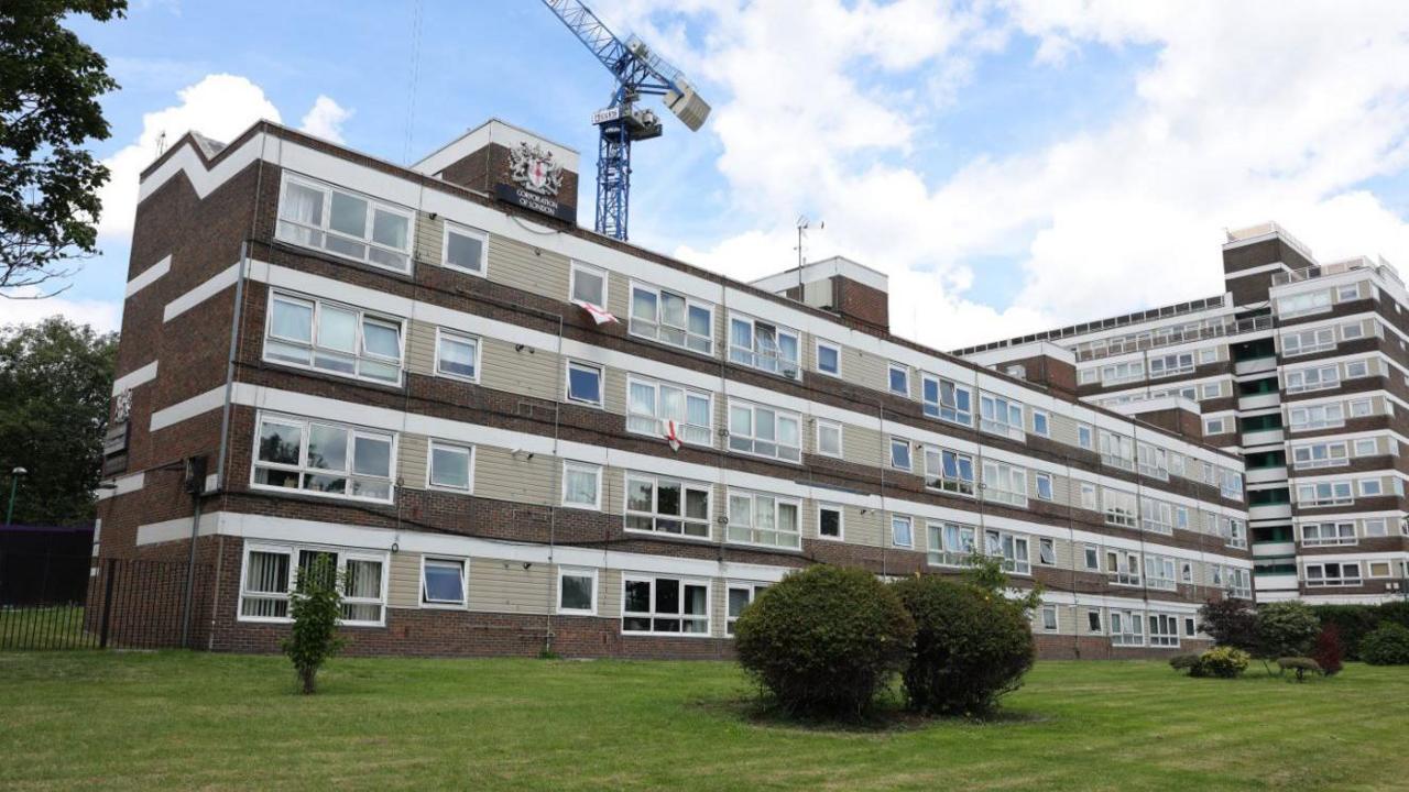 A general view of the block of flats, which are made of brick and light brown cladding with a City of London Corporation sign fixed on the roof