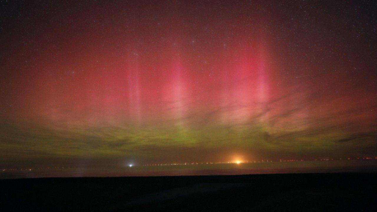 Red and green colours light up the sky over the dark land in the foreground