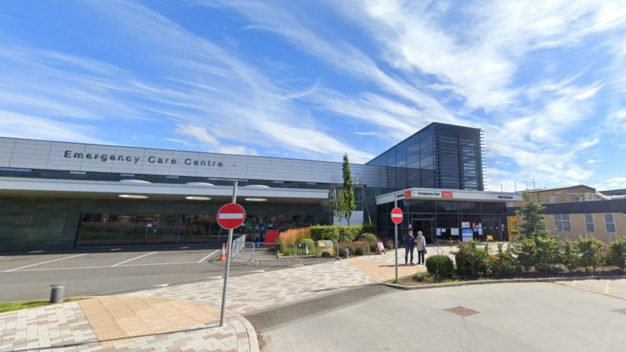 A&E at Queen Elizabeth Hospital, Gateshead. It is a sunny day. The photo shows a grey building with the sign "Emergency Care Centre".