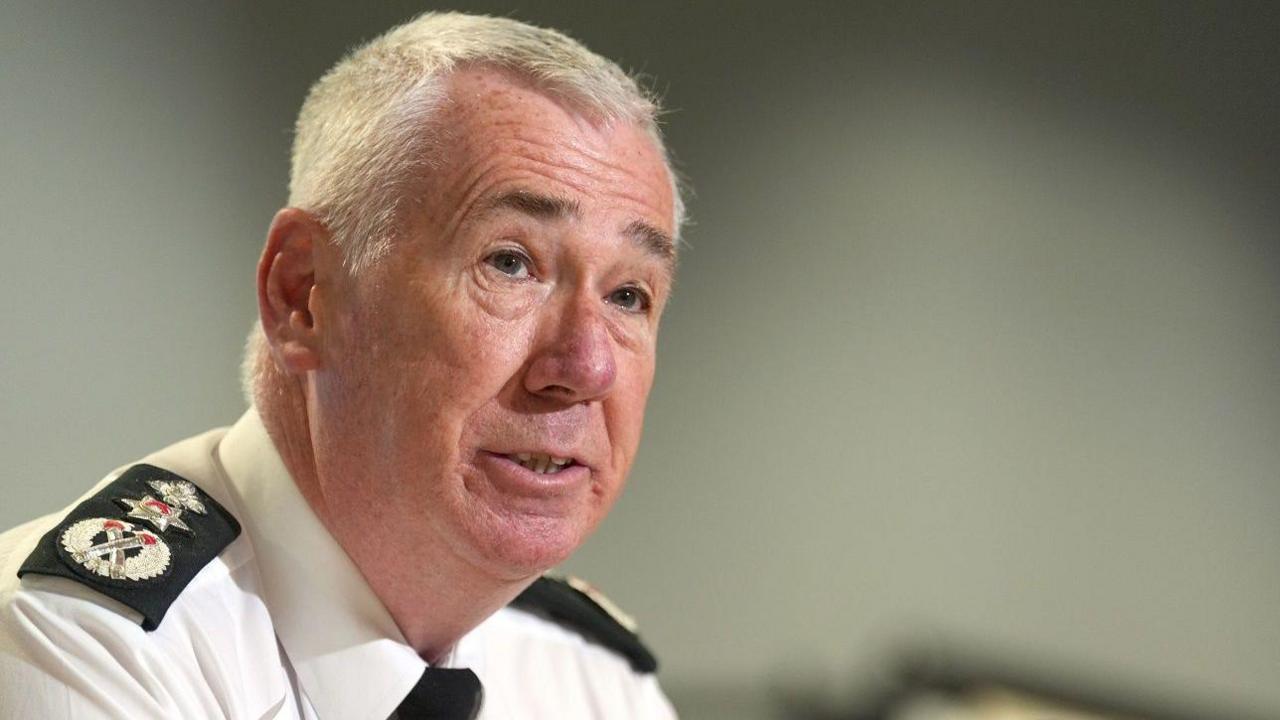 Jon Boutcher speaks to reporters while wearing his PSNI uniform. He has short white hair and dark eyebrows.