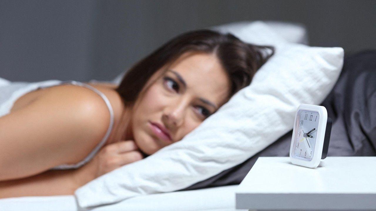 A woman with dark hair lying on a pillow starring at an alarm clock