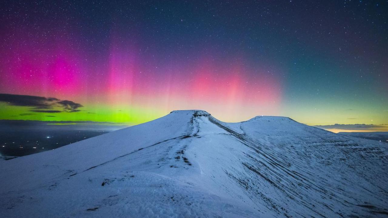 The peaks of Pen y Fan and Corn Du in Bannau Brycheiniog (the Brecon Beacons) covered in snow. The skies behind are bright pink and green.