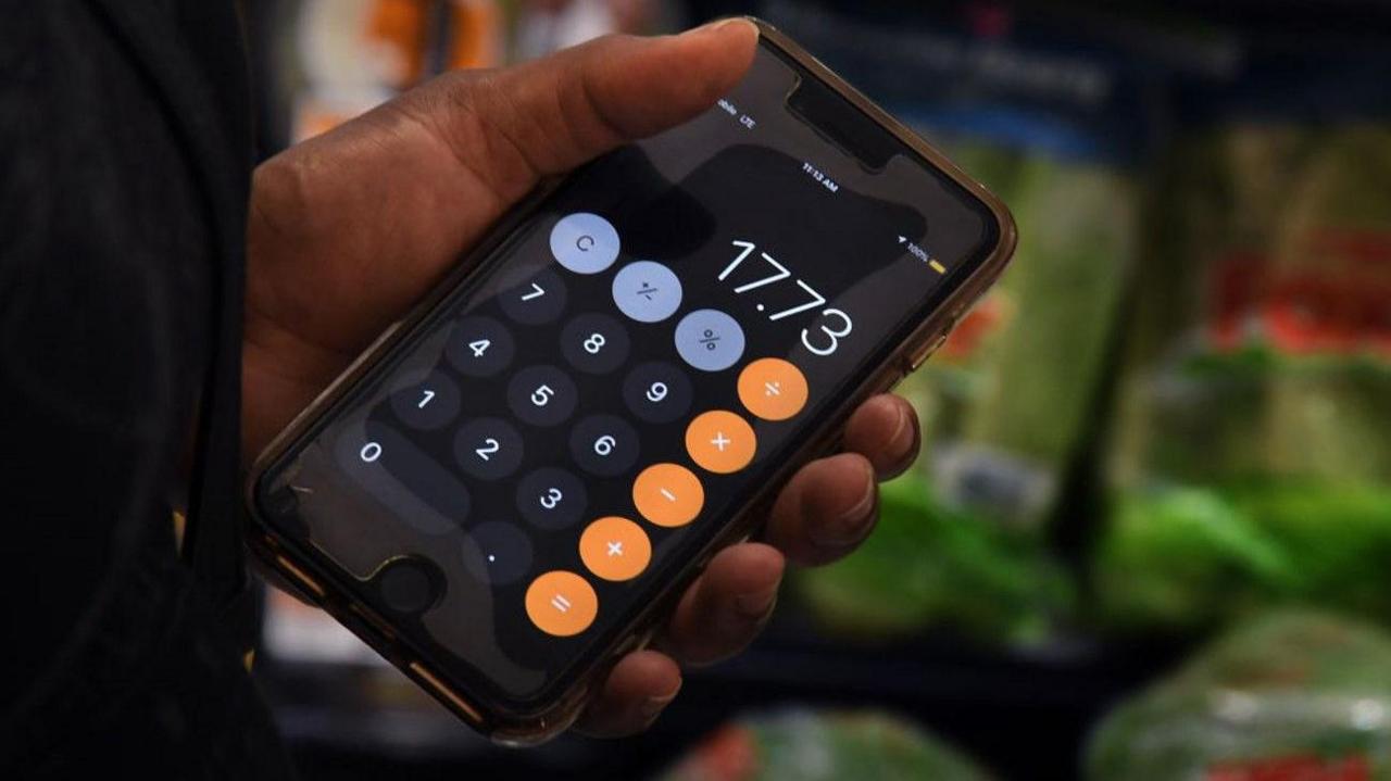 Someone's hand is holding a screen showing a calculator. The background is blurred.