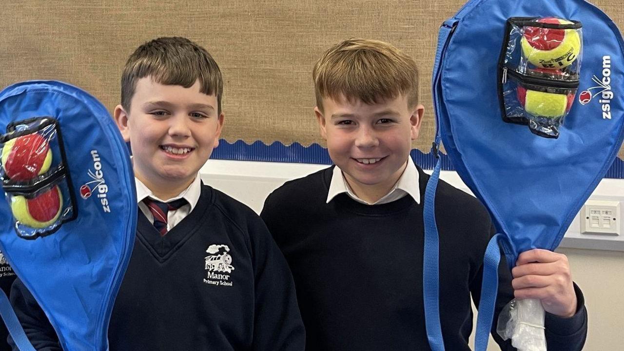 Two schoolboys smiling with their tennis tackets.