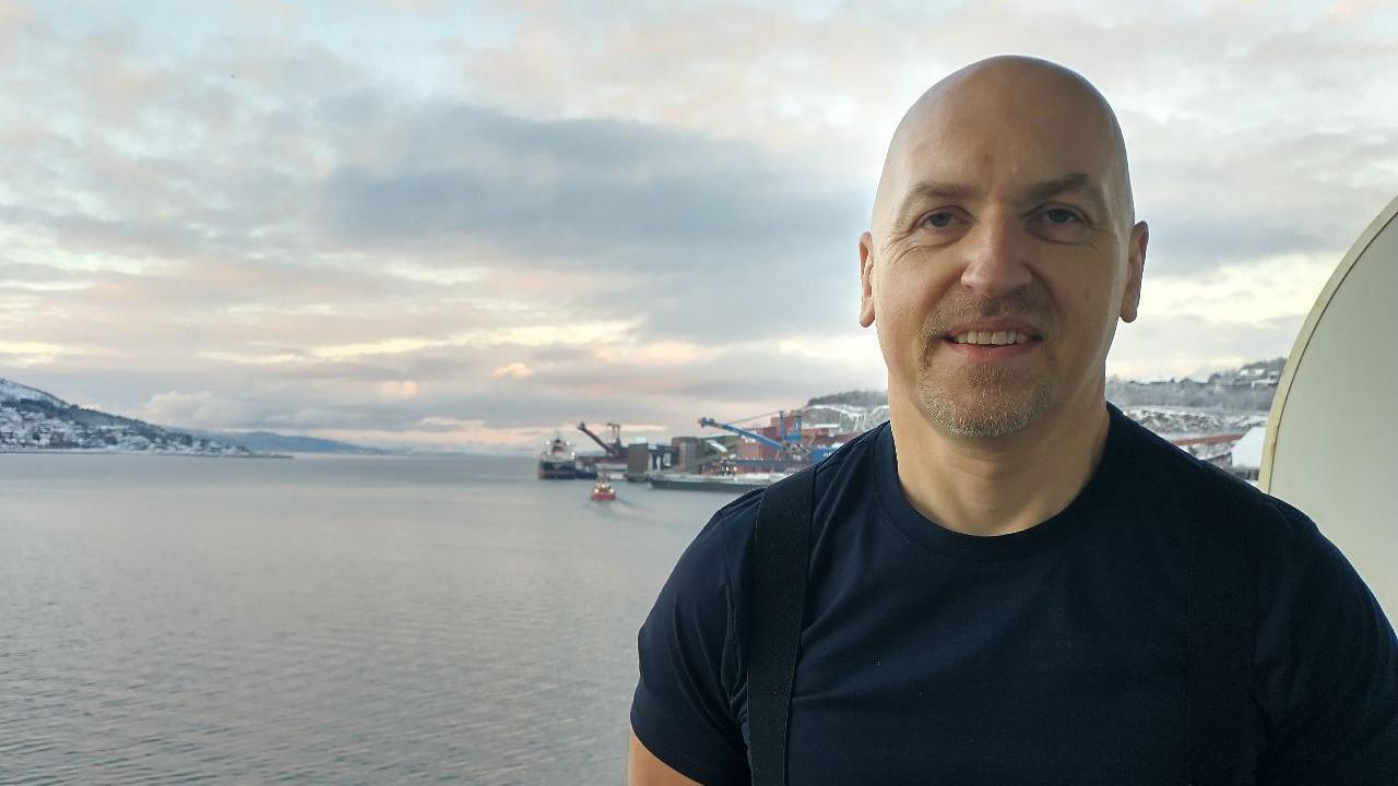 Mick Hull standing in front of a body of water with a port in the distance