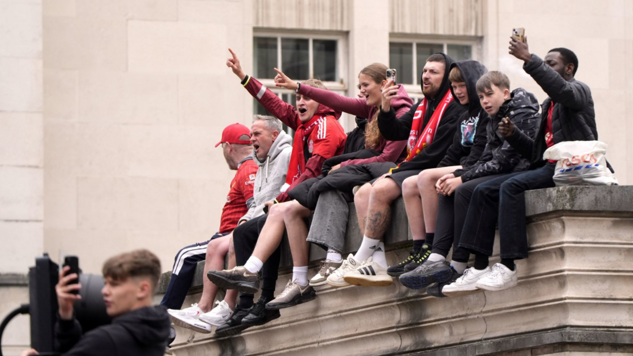 Liverpool supporters sitting in a line along a wall