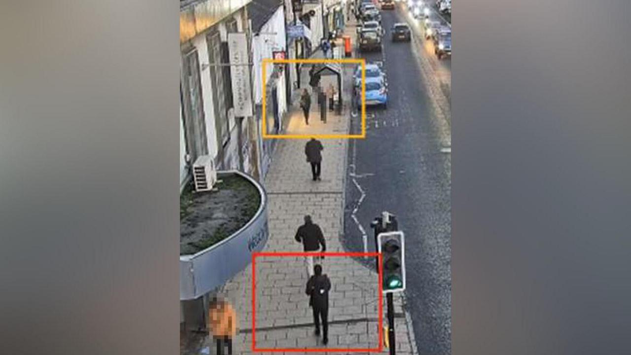 A CCTV still showing several people walking down a street. A yellow box has been drawn around Holly Newton at the top of the picture and a red box around the teenage defendant who is a short distance behind her