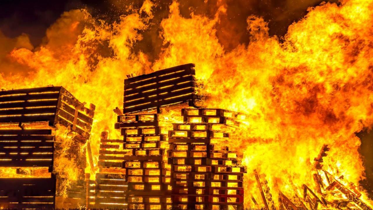 A large fire with wooden pallets visible in the flames