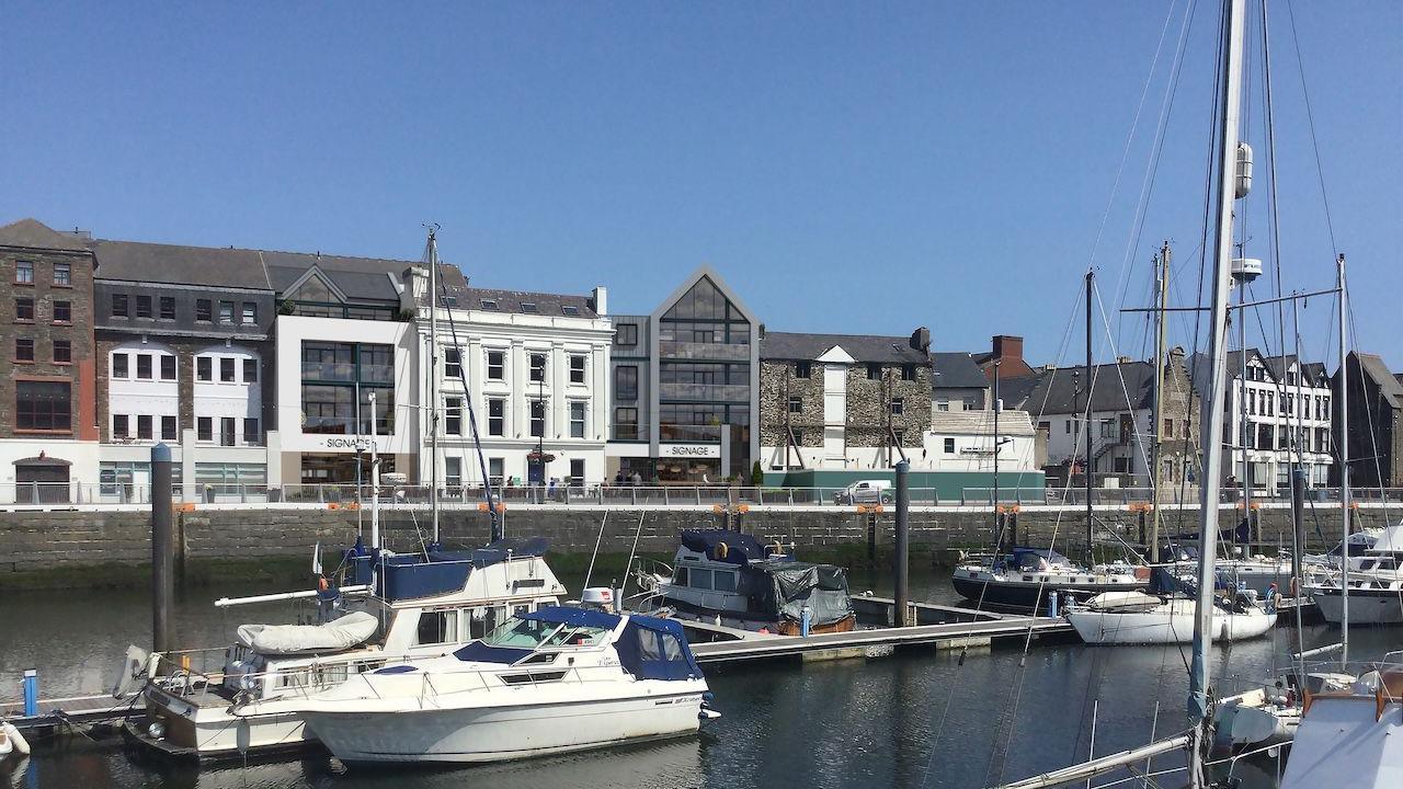 A view from across the harbour two modern buildings are on either side of a white Victorian building, scaffolding remains on the right of the new development.