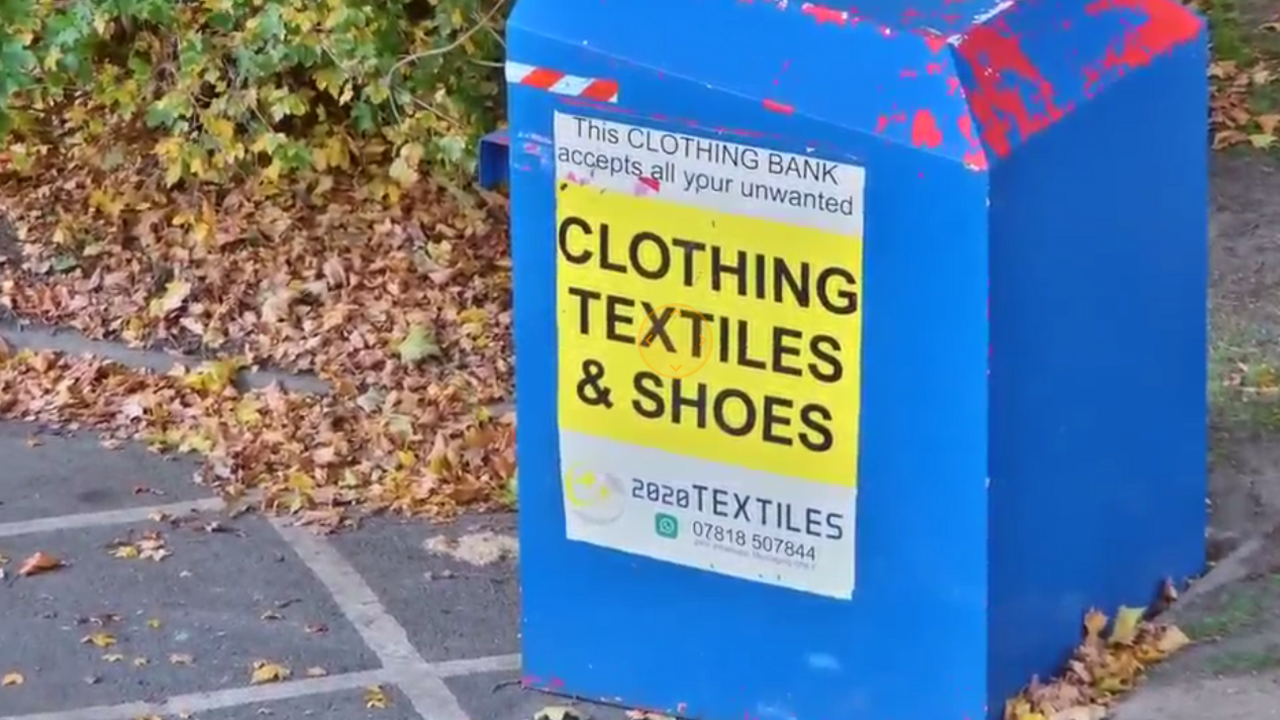 A large blue box-shaped bin in a car park labelled 'clothing textiles & shoes'.