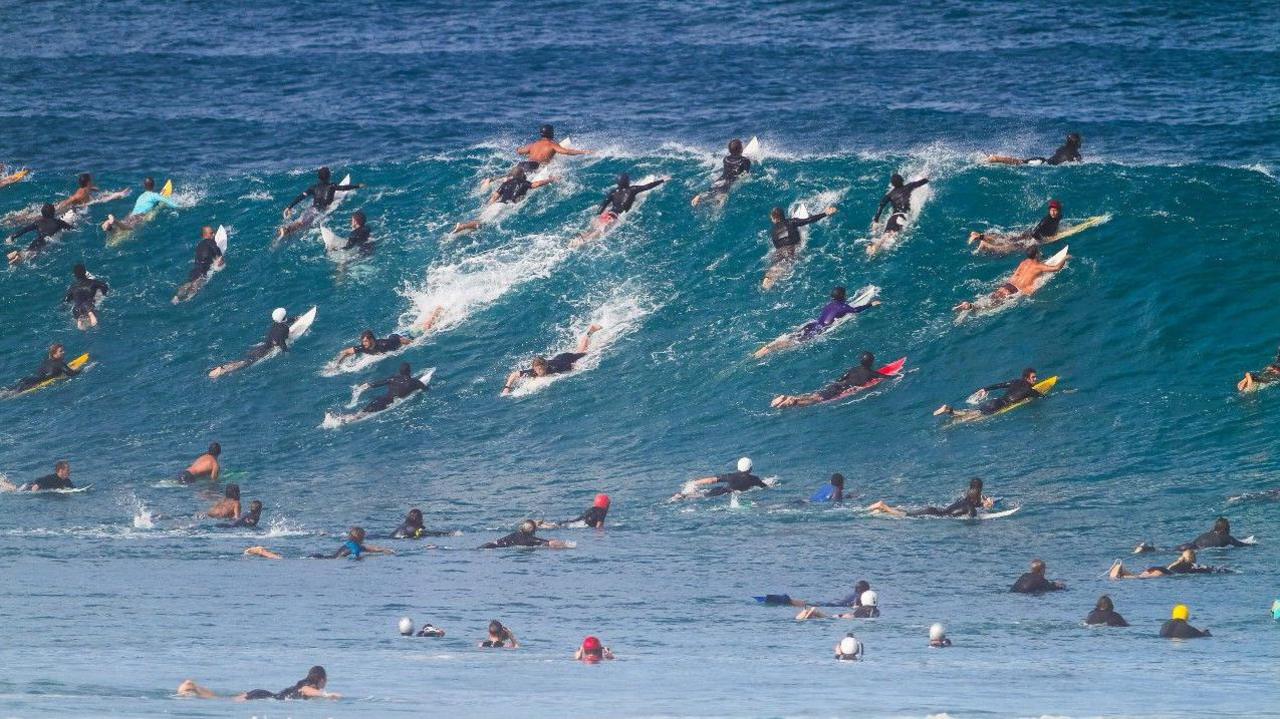 Dozens of surfers and photographers vying for position to catch a wave at Pipeline in Hawaii