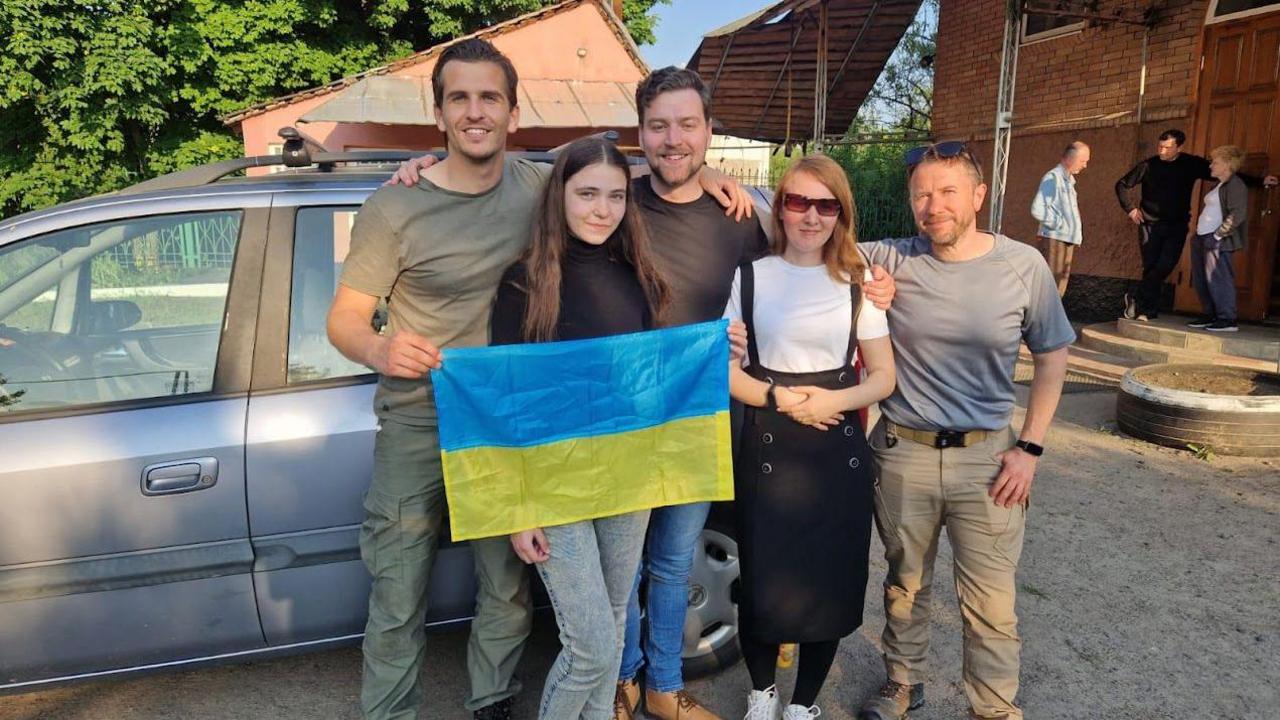 A group of people holding a Ukrainian flag in the centre huddle together for a picture. Ben Allen stands to the right.