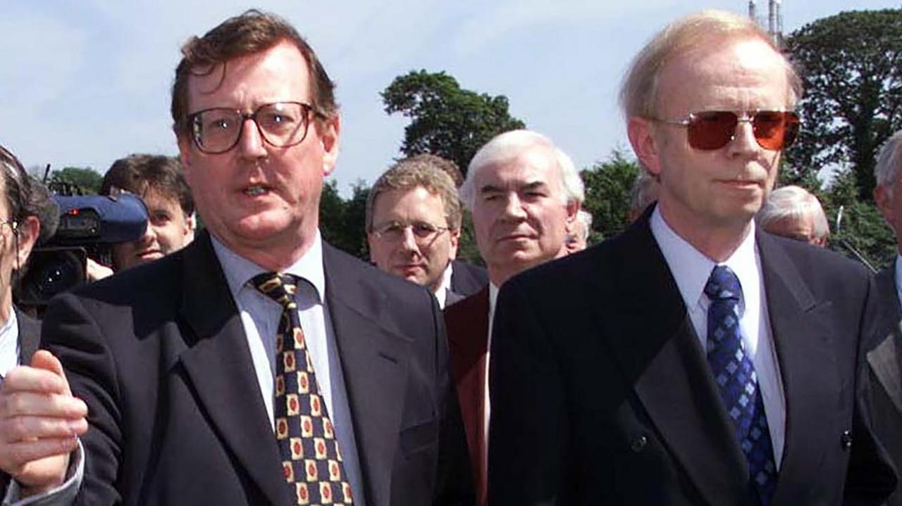 David Trimble on left of picture in a navy suit gesturing towards the camera. He has brown hair and glasses. 
Lord Empey on the right is also in a navy suit. He has blonde hair and is wearing sunglasses