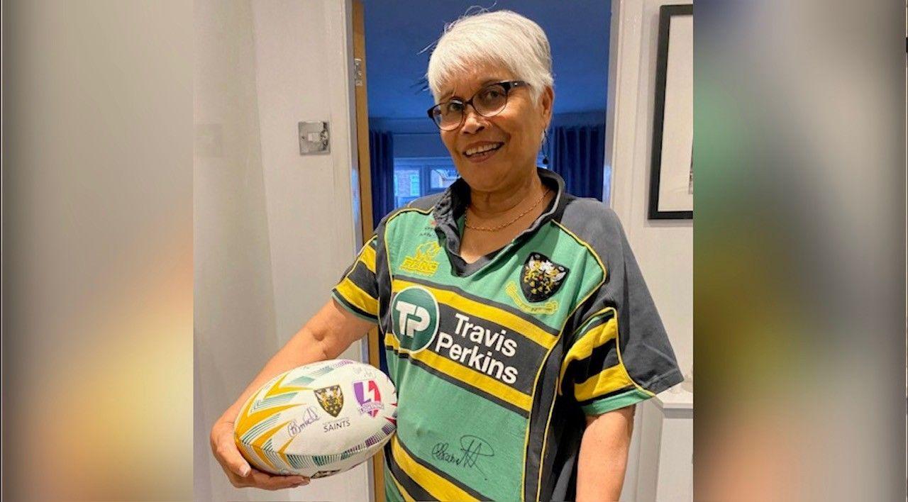 Aurora with short blond hair wearing a Saints shirt and carrying a rugby ball