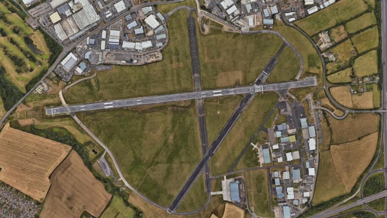 An aerial view screenshot from Google maps. It shows Gloucestershire Airport and two long runways amidst fields of grass.