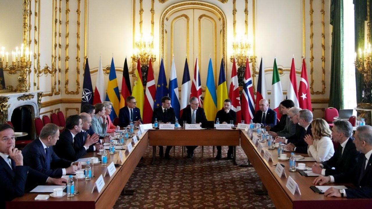 The 18 world leaders gathered around a U-shaped table with their countries' flags behind them in a room with white walls and gold detail. Sir Keir Starmer is sitting in the centre with Emmanuel Macron and Volodymyr Zelensky flanking him.