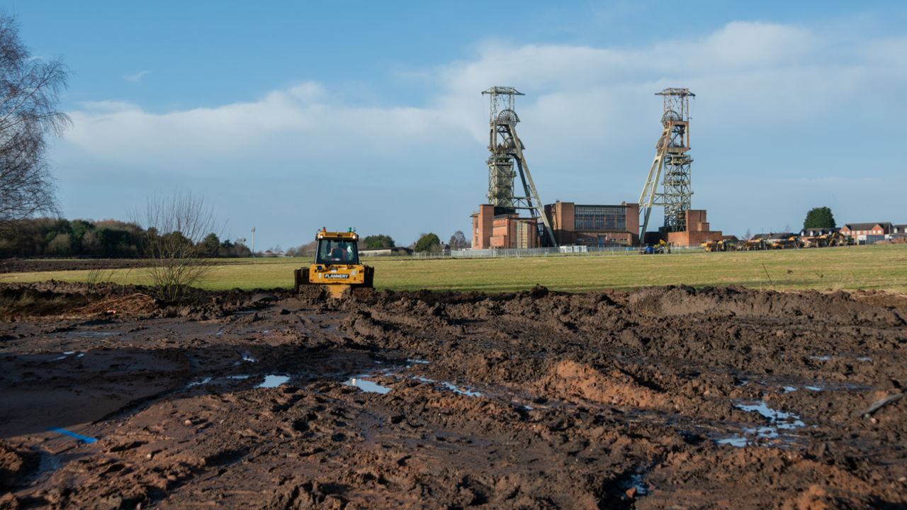 A yellow digger working at a mud filled site with Clipstone Colliery headstocks in the background