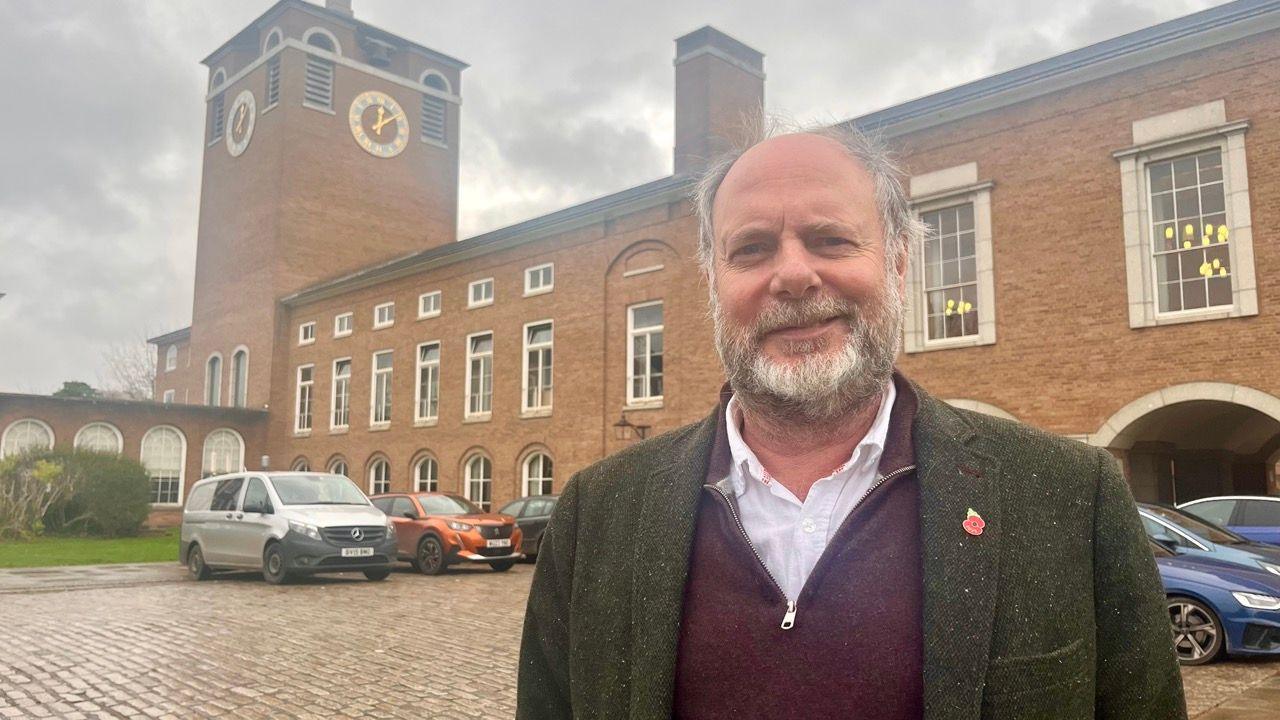 Julian Brazil in a white shirt, a burgundy quarter-length zip sweater and a gree blazer and wearing a poppy badge.