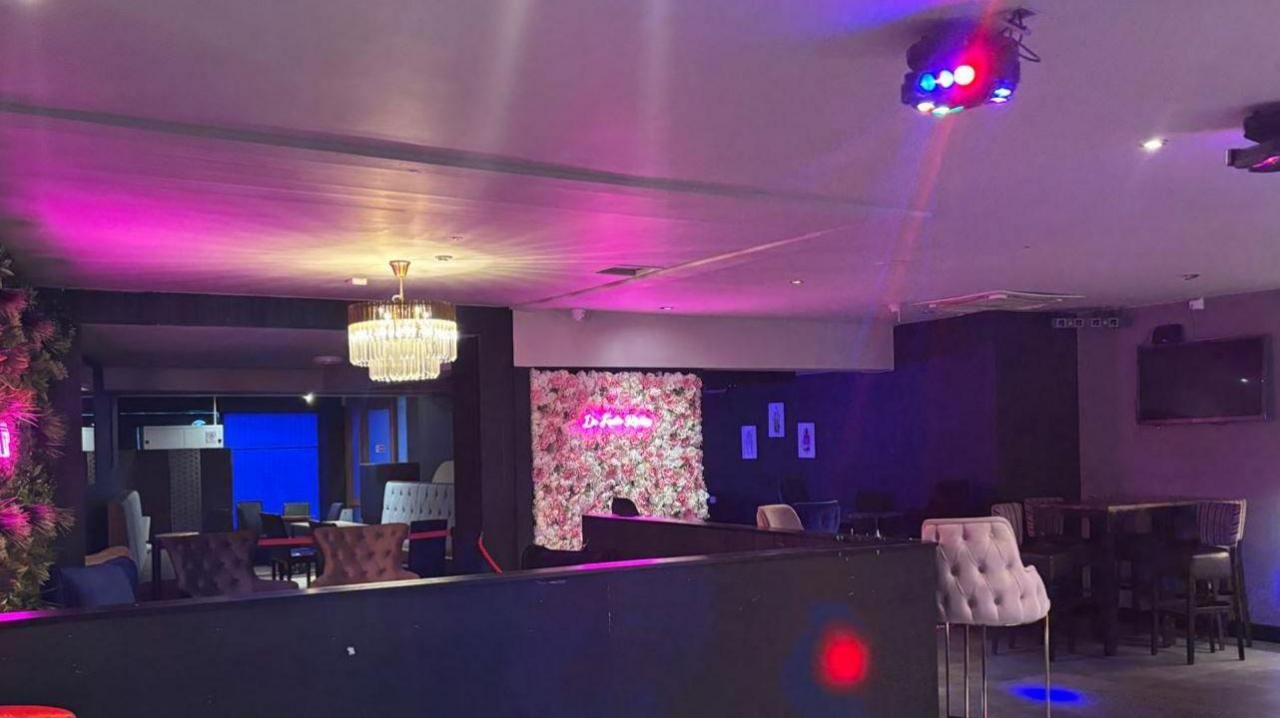 Inside DeFacto nightclub in Ripon with a bar to the right, disco lights, chairs and bar stools, neon lighting features, and a chandelier