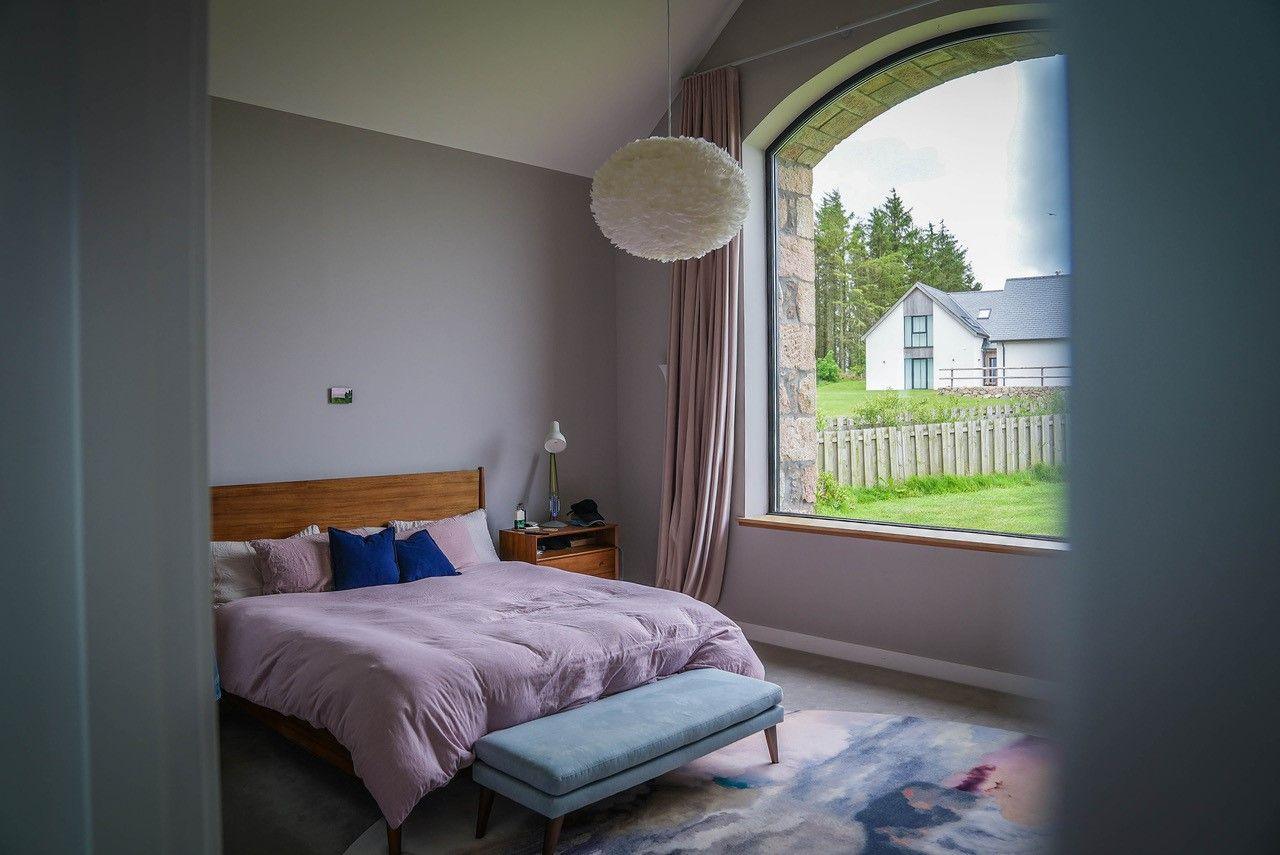 One of the double bedrooms, with a pale pink duvet and contrasting blue cushions, a pale blue chaise and a pretty blue and pink rug, but the window again is the star attraction, framing the countryside outside