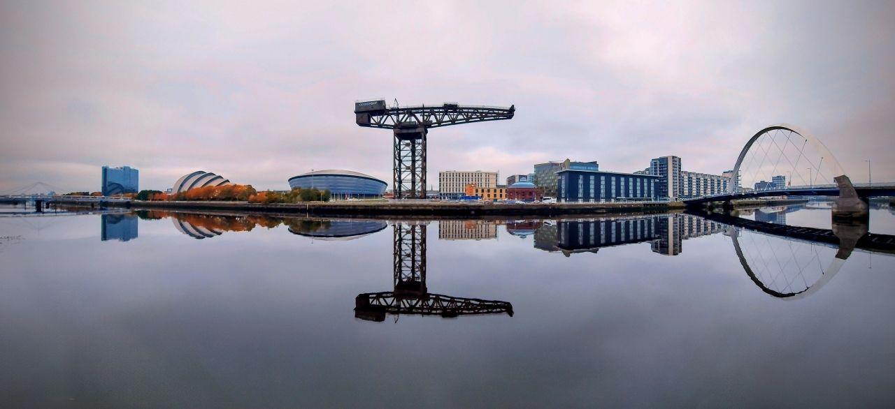 Bridges, buildings and a large decommissioned crane are reflected in the still waters of the River Clyde