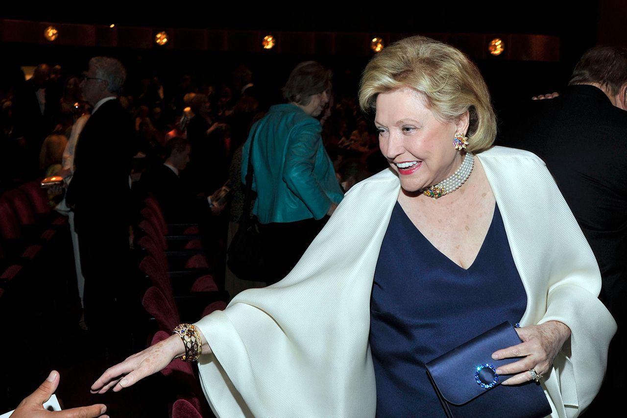 Barbara Taylor Bradford reaches out a hand to greet someone out of frame, while wearing a white shawl and blue clutch handbag at the Literacy Partners Evening of Readings Gala at David H. Koch Theater on May 10th, 2010 in New York City