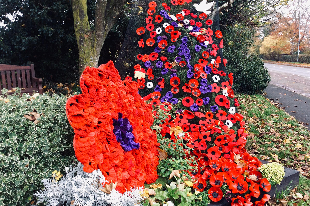 A display of knitted poppies in Gnosall. They are cascading down into a flower bed, with a larger wreath to the left of the photo. 