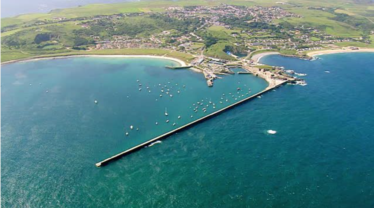 Alderney harbour with a wide expanse of blue see surrounding the green coast