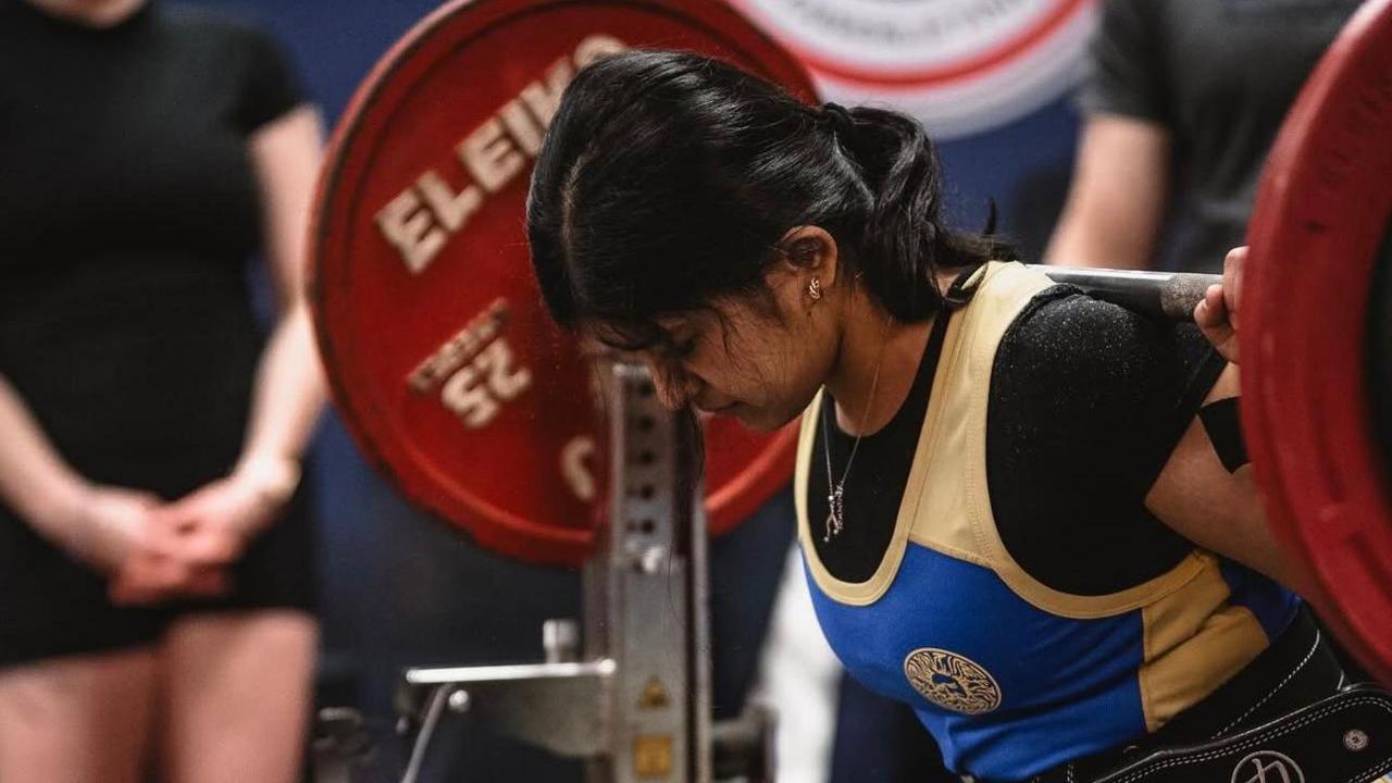 A woman balancing a barbell on her upper back with two red plates on either side, both 25kg, preparing to squat in a competition.