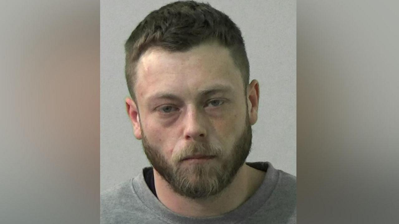 Mugshot of a man with a dark beard and hair