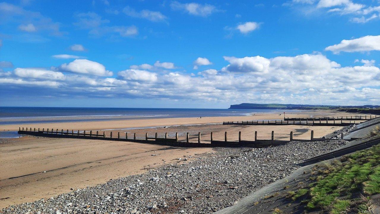 empty sandy beach showing beach groynes, sea, under a cloudy, blue sky