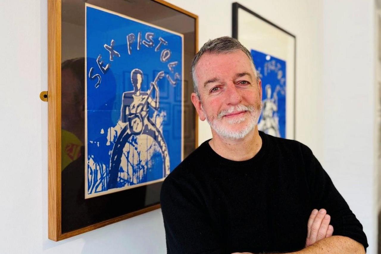 David McCracken, man with arms folded, smiling at camera, in front of Sex Pistols artwork.