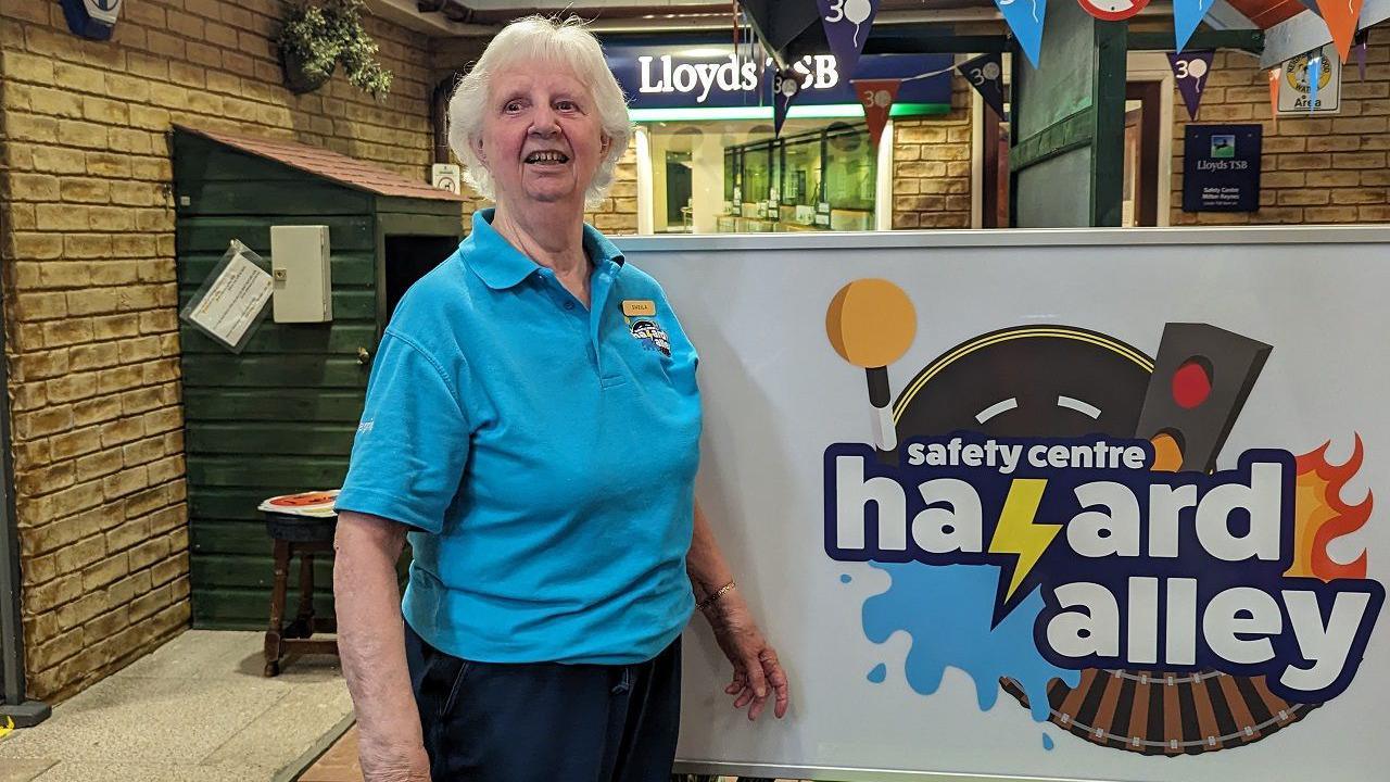 Sheila Cutler is standing in the entrance part of Hazard Alley near a mock Lloyds Bank