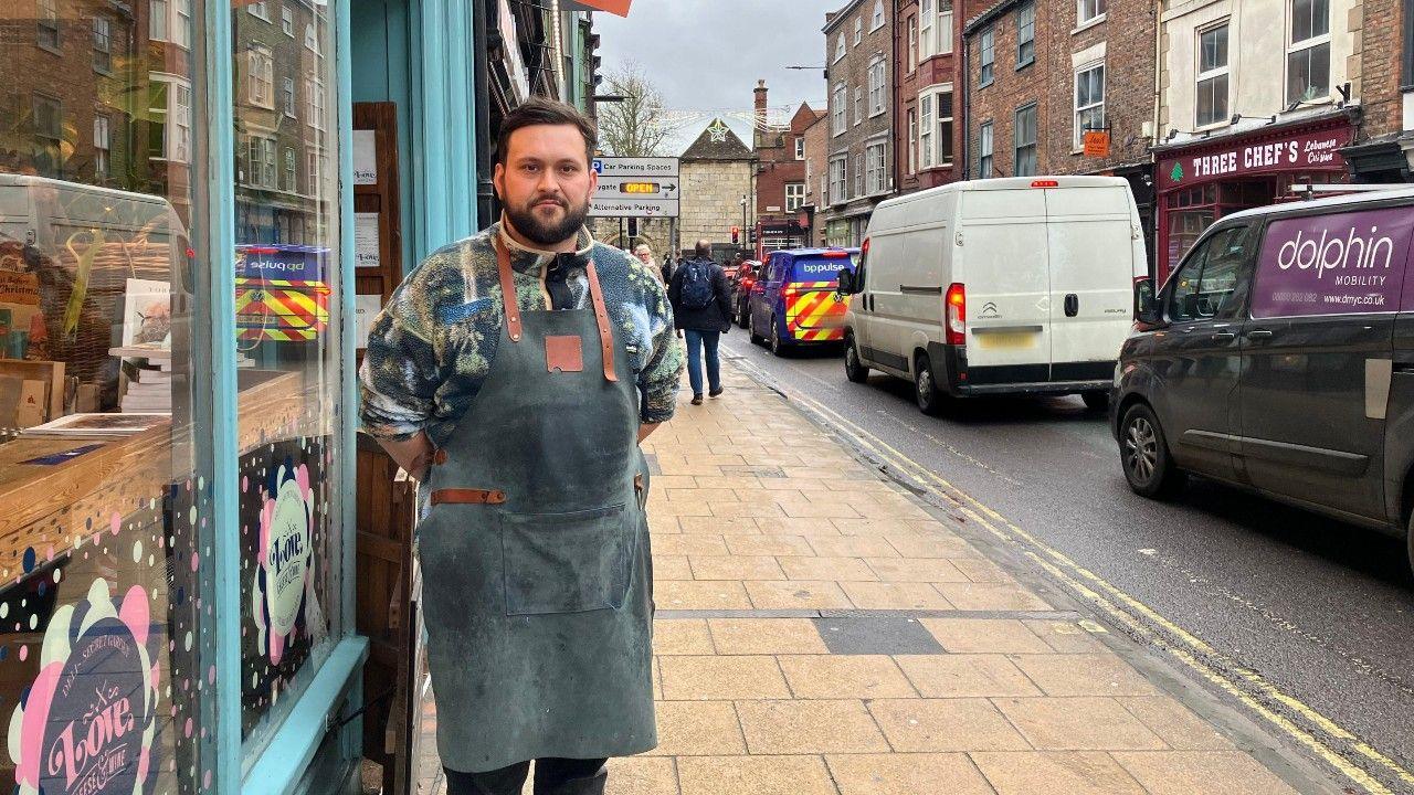 Jordan Thomson, owner of Love Cheese on Gillygate with queuing traffic next to him