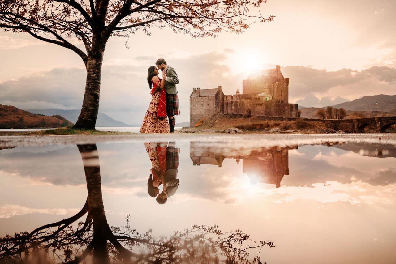 A couple standing in a field before a castle