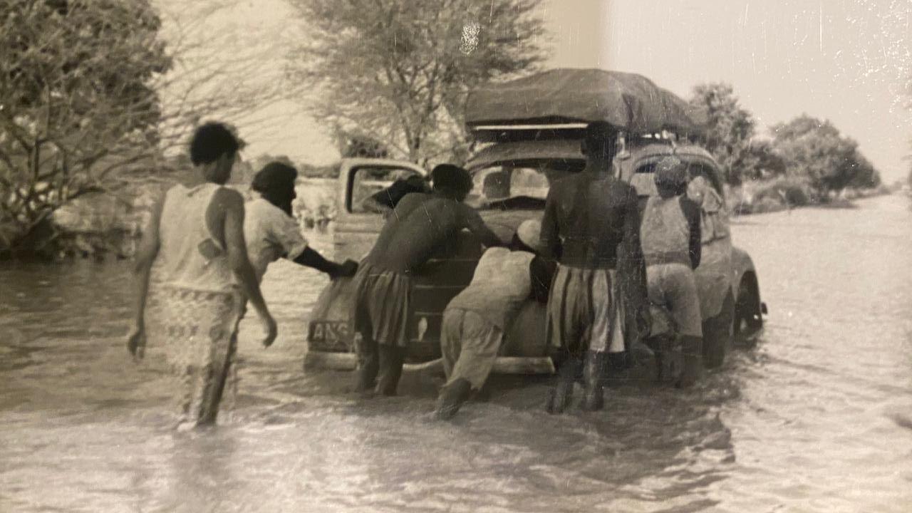A historical photo of local villagers in India helping push the Ford V8 motor car up a flood-hit road