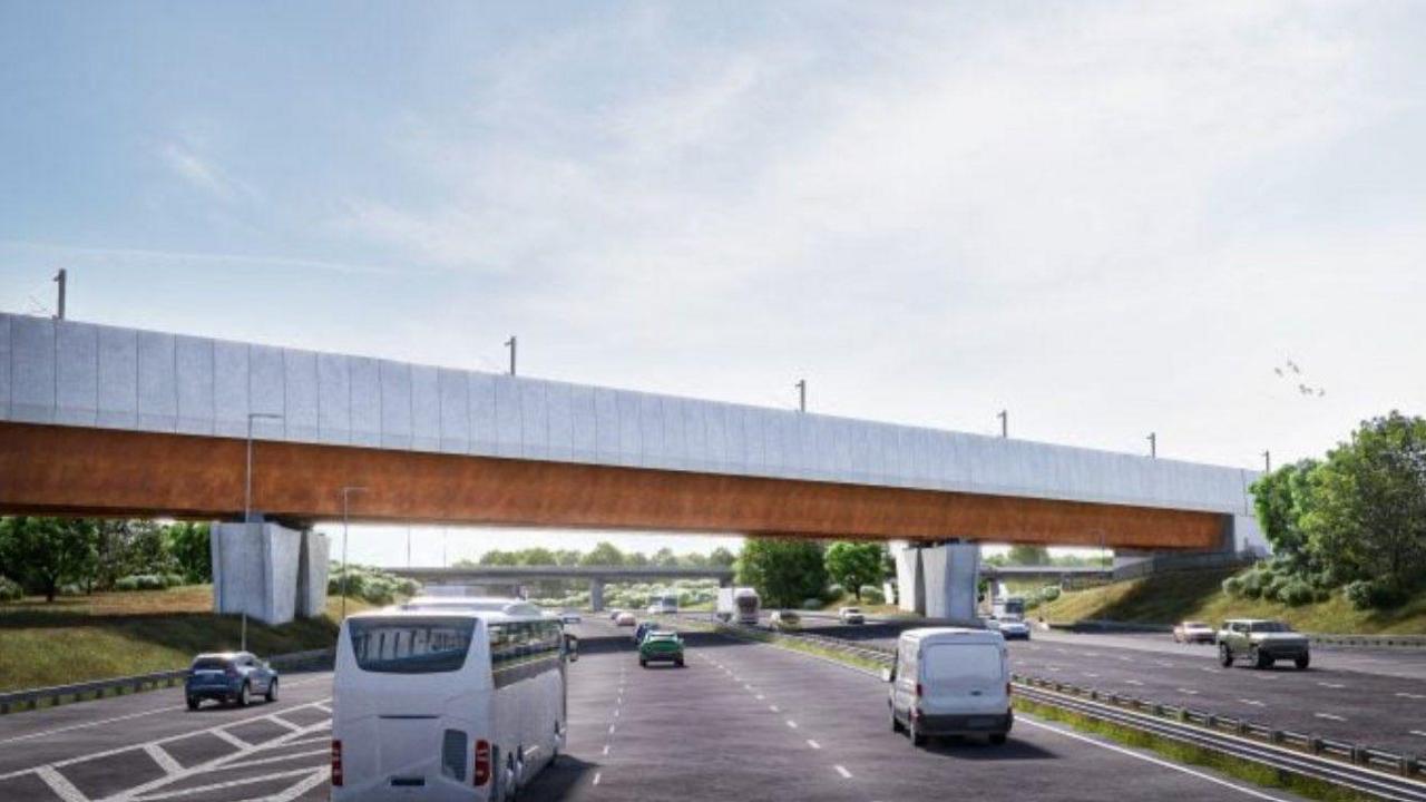 A white and brown viaduct is over the motorway in the background. In the foreground is a slip road on the left, three lanes in the middle of the photo and other lanes with traffic going in the opposite direction on the right hand side.