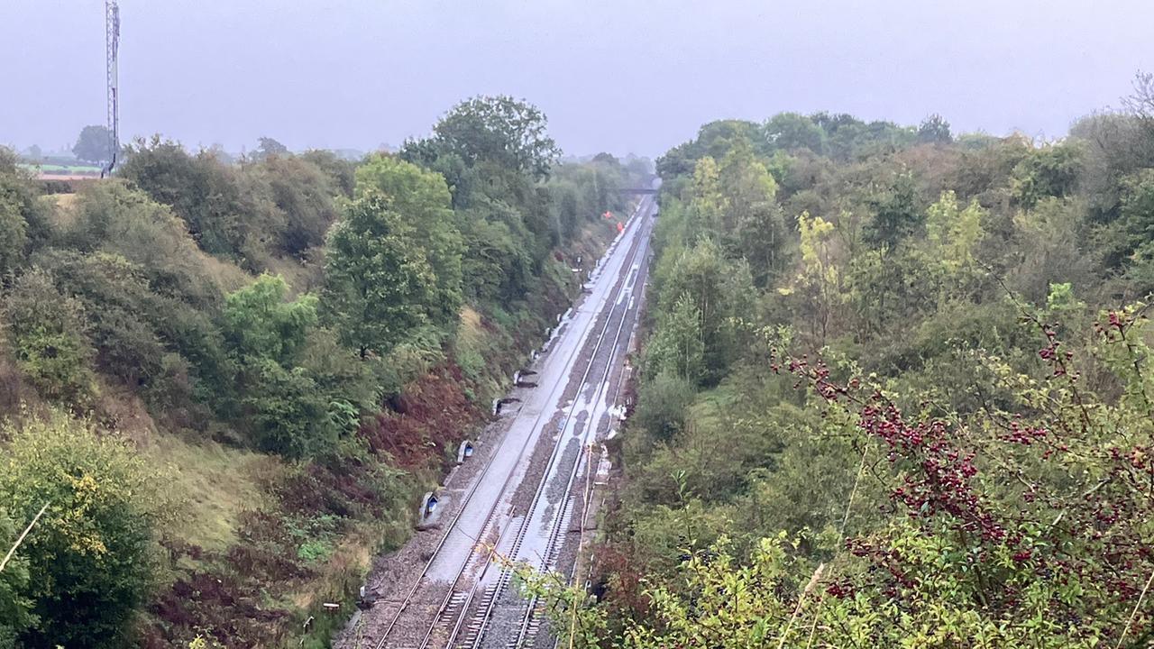 A rail line in between two large grass verges. The tracks are partially submerged by water in some parts.