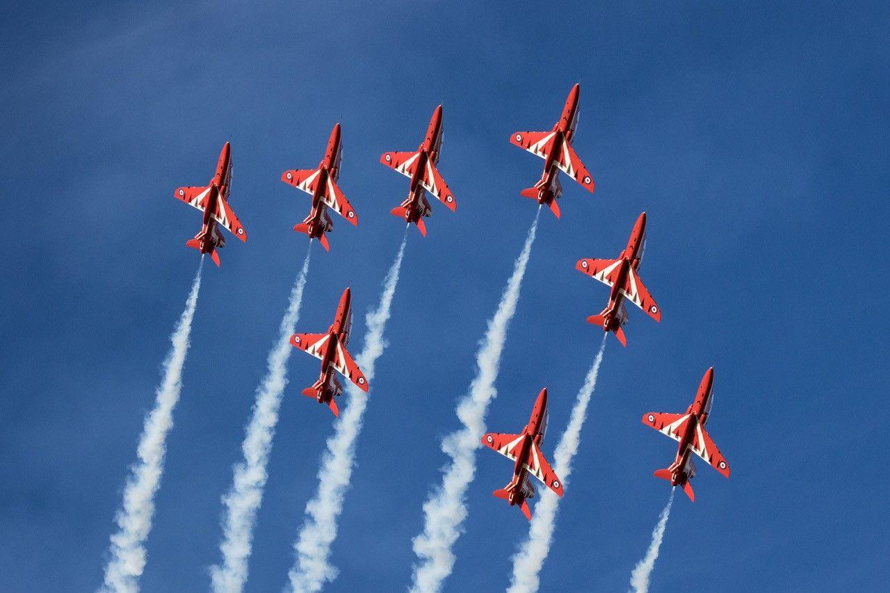 Eight Red Arrow planes flying against a clear blue sky with white smoke trails in the wake of each plane