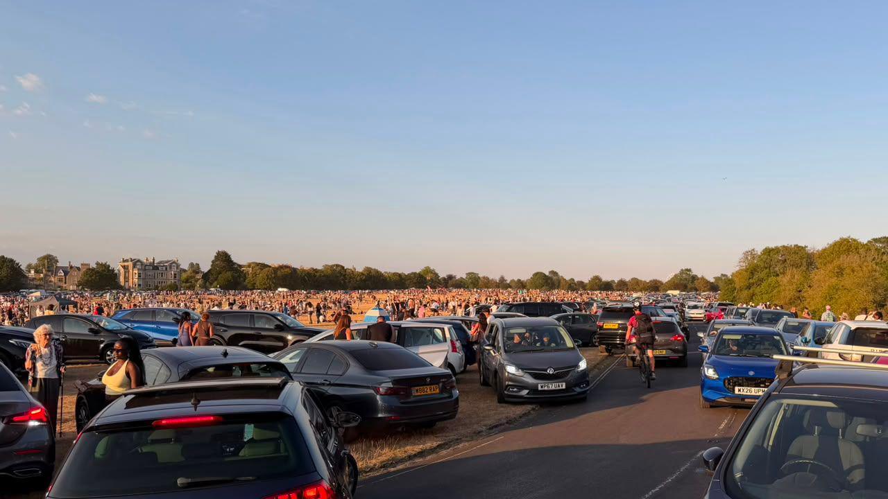 Big crowd sitting on grass near parked cars on Clifton's Downs.