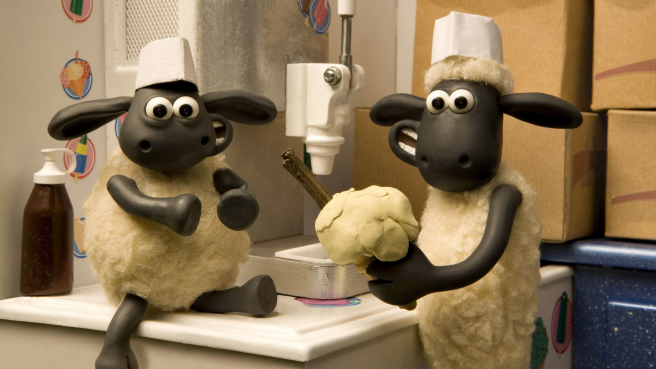 Two clay animation sheep are in an ice cream van. Timmy is sat ont he counter while Shaun holds a traditional vanilla ice cream with a flake in a cone.