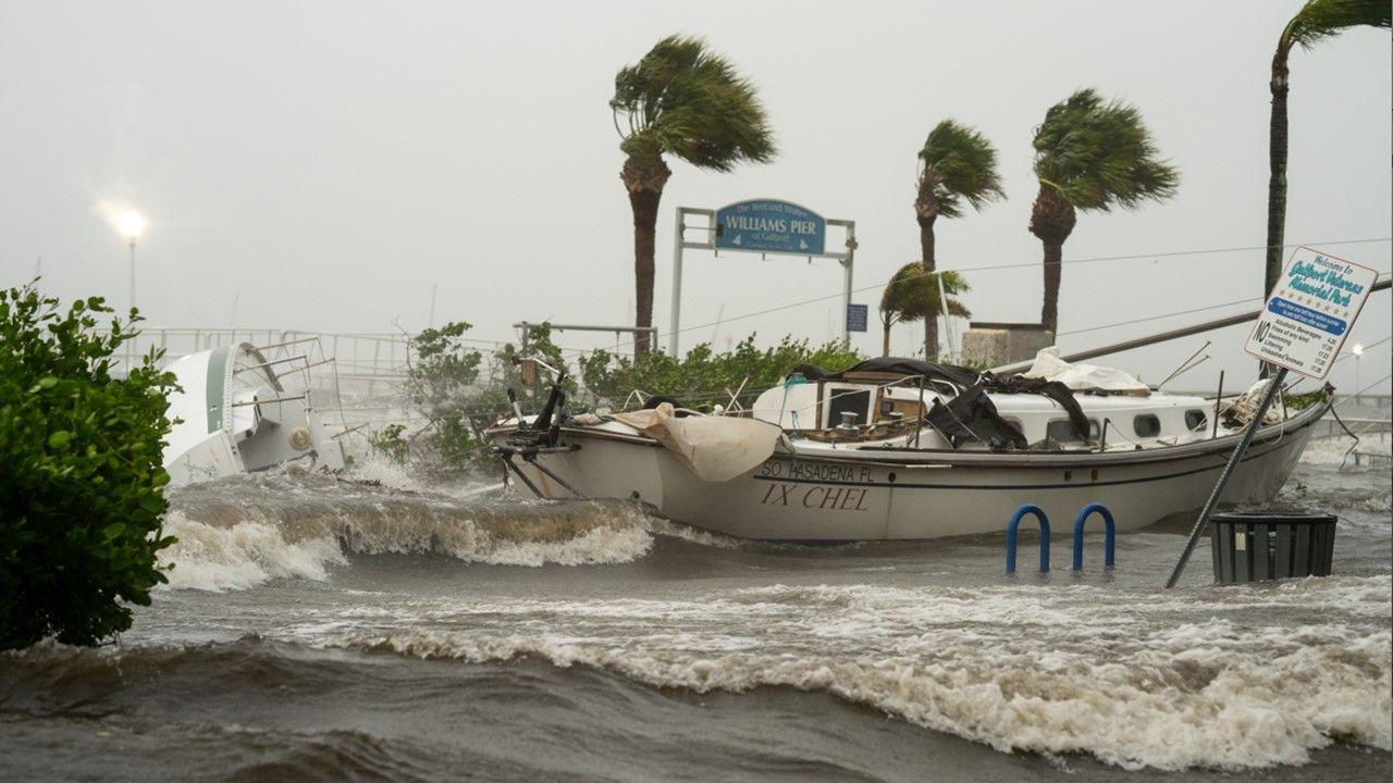 The sea crashes around a small boat and onto land in Florida with Palm trees behind in gusty wind