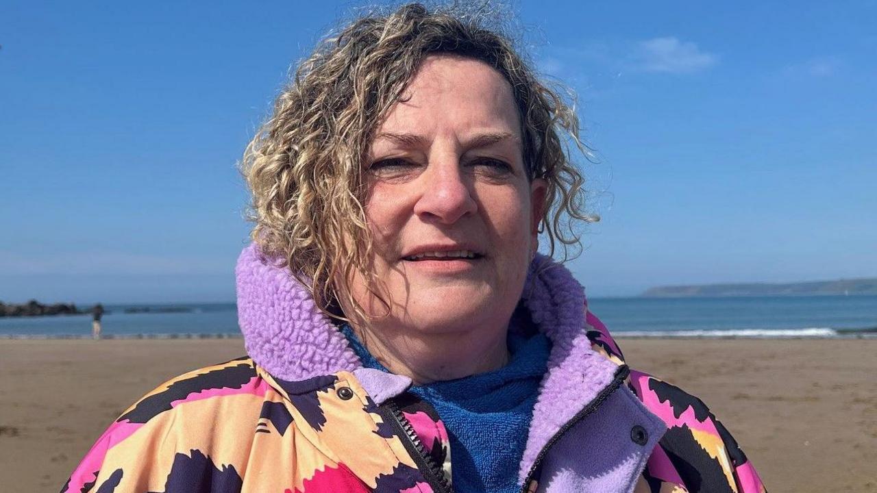 Lucy Bennett with blonde curly hair wearing a purple and pink patterned dry robe