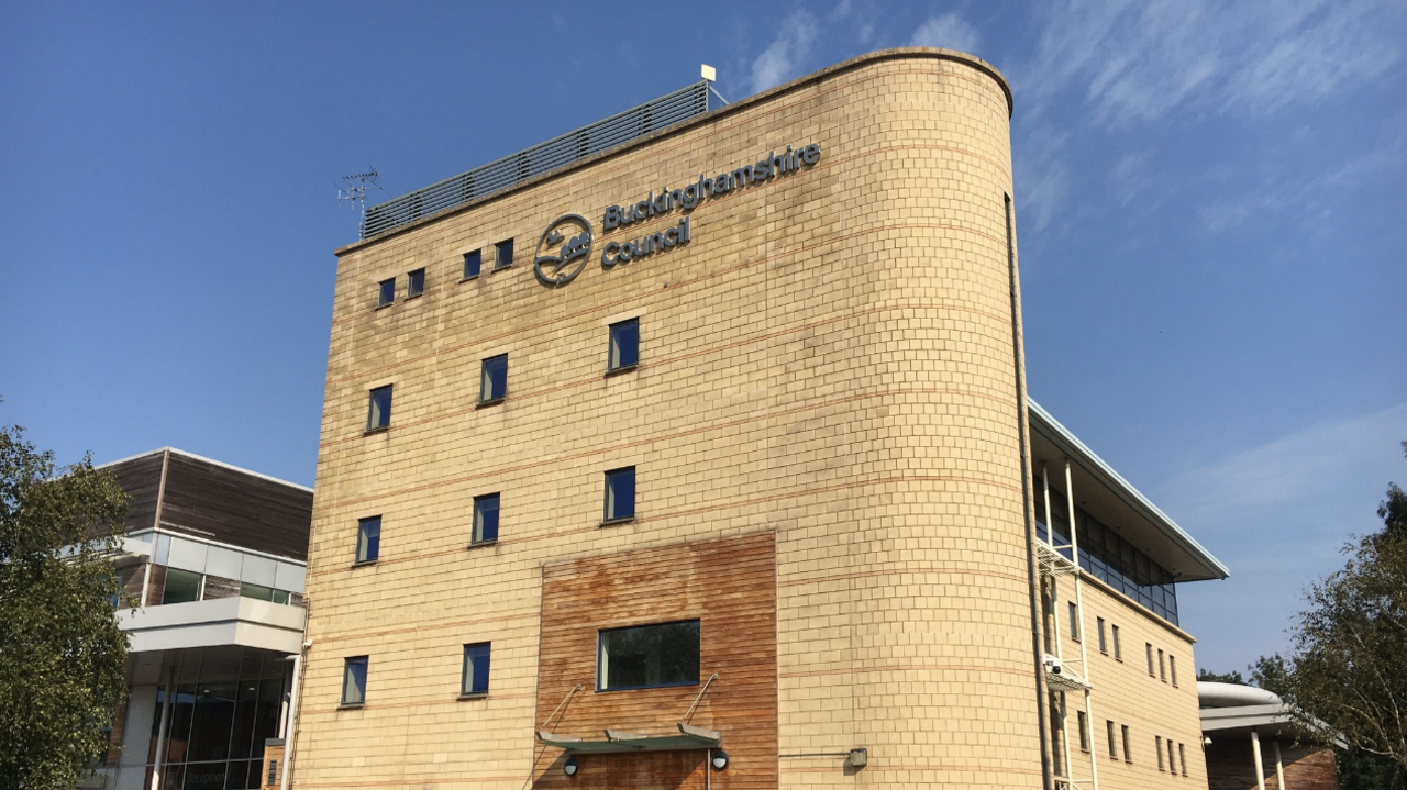 A picture of the Buckinghamshire Council headquarters in Aylesbury. It is a light yellow brick building on four floors and there is blue sky behind it.