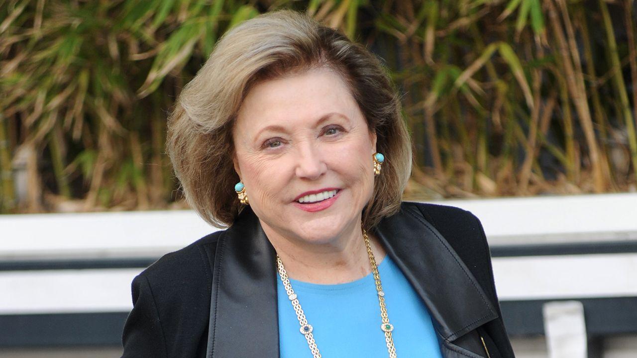 Barbara Taylor Bradford smiles and looks at the camera while wearing a black suit and blue top outside, pictured in London in 2015