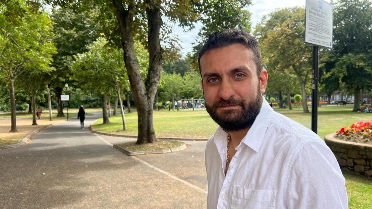 Bobby Yordanov is wearing a white shirt, he has a dark brown beard and dark brown hair.