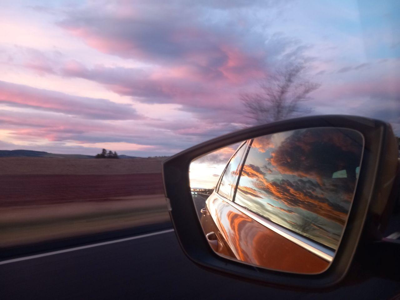 A car mirror reflecting a sunset with a landscape in the background