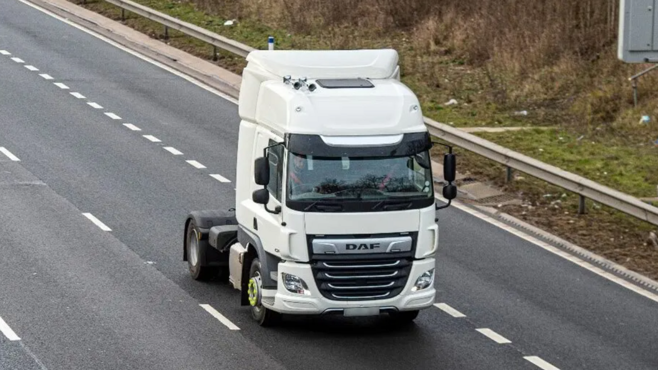 A white lorry cab driving on a road with multiple lanes. There is a metal barrier on one side of the road.