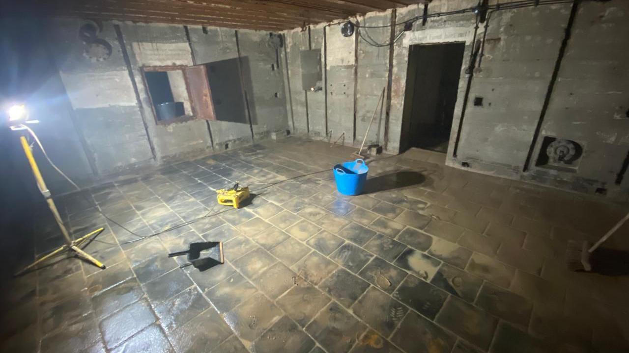 Inside a German World War Two bunker. A blue bucket is on the tiled floor along with a large large and an extension cable.